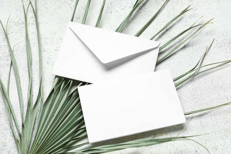 Envelope with blank card and dried palm leaf on white background