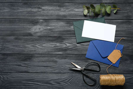 Envelopes with card, scissors, eucalyptus and rope on dark wooden background