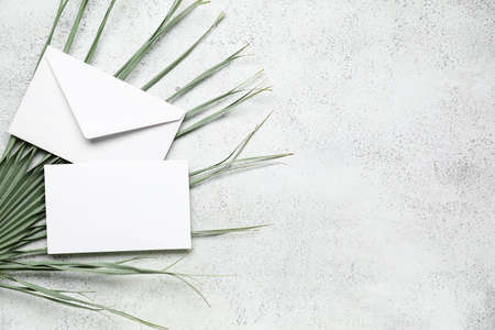 Envelope with blank card and dried palm leaf on white background