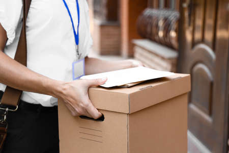 Young postwoman with letters and box outdoors, closeup