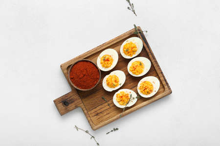 Board with tasty stuffed eggs, paprika and thyme on white background. easter celebration