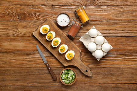 Board with stuffed eggs, spices, knife and green onion on wooden background. easter celebration