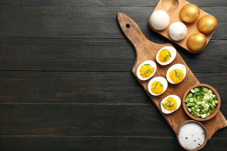 Board, holder with Easter eggs, spices and green onion on dark wooden background. easter celebration