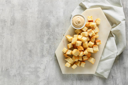 Board with crunchy croutons and bowl of tasty sauce on tableの写真素材