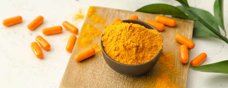 Turmeric pills and bowl with powder on light tableの写真素材