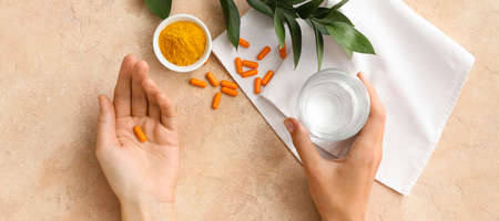 Female hands with turmeric powder pills and glass of water on color background, top viewの写真素材