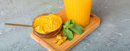 Bowl of turmeric powder and glass of healthy drink on grunge background