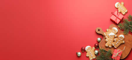 Tasty gingerbread cookies and Christmas decor on red background with space for text