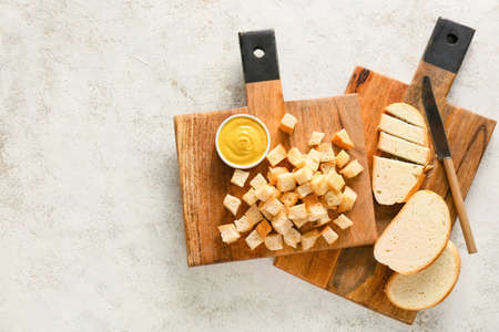 Boards with tasty croutons, bread slices, knife and sauce on light background