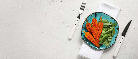 Plate of tasty baked carrots, spinach and cutlery on light background with space for textの写真素材