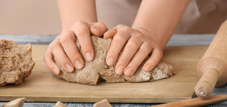 Baker kneading fresh dough in kitchen, closeup