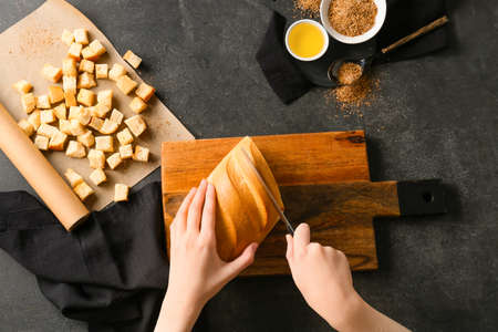Woman cutting fresh bread for croutons on black backgroundの写真素材