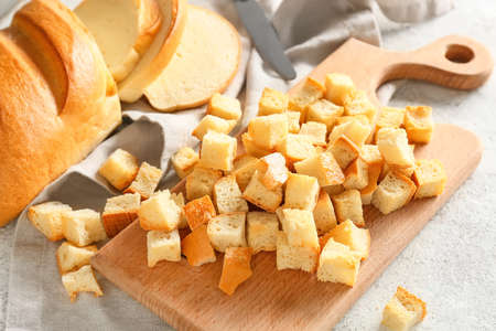 Board with tasty croutons, loaf of bread and napkin on light background, closeupの写真素材