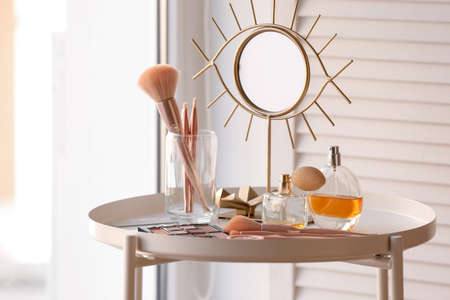 Holder with makeup brushes, cosmetic products and mirror on table near windowの写真素材