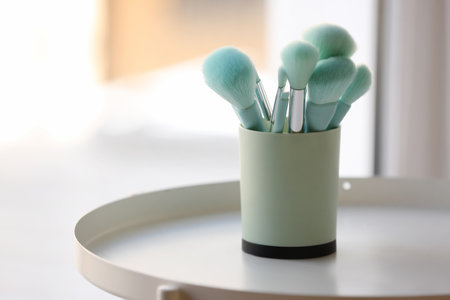 Holder with blue makeup brushes on table near windowの写真素材