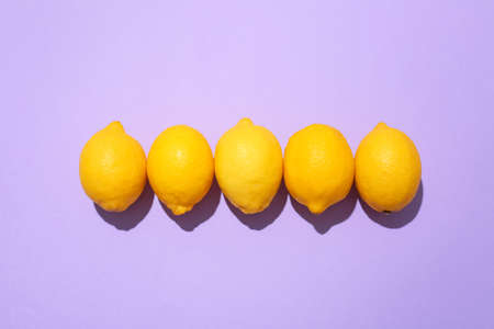 Row of ripe lemons on lilac background, top view