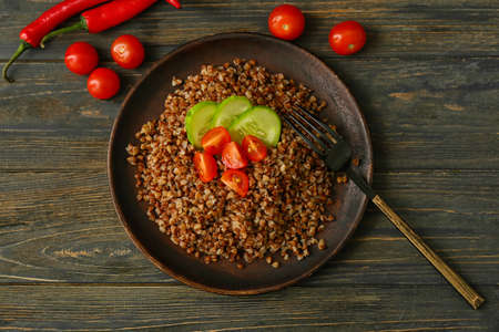 Plate of tasty buckwheat porridge with vegetables on wooden table, top view