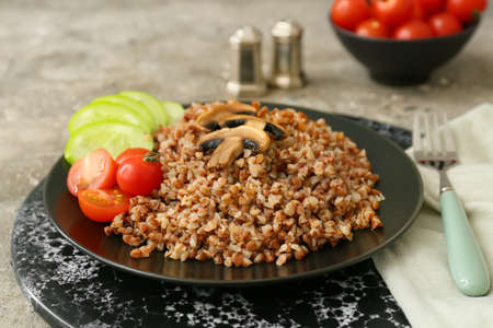 Plate of tasty buckwheat porridge with vegetables and mushrooms on gray tableの写真素材