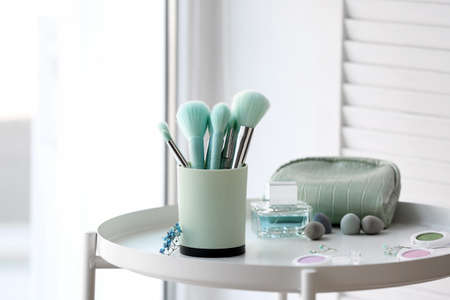 Holder with makeup brushes and cosmetic products on table near windowの写真素材