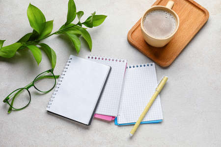 Notebooks, cup of coffee, glasses and pen on light background