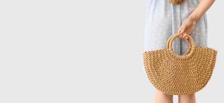 Elegant young woman with rattan bag on light background with space for text, back viewの写真素材