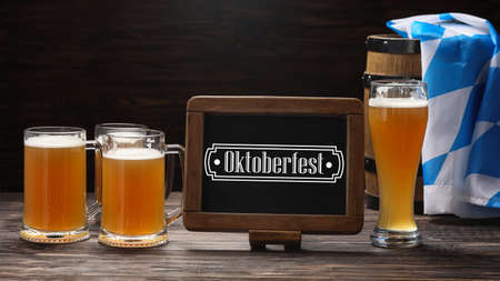 Glass and mugs of cold beer and chalkboard on table. Oktoberfest celebrationの写真素材