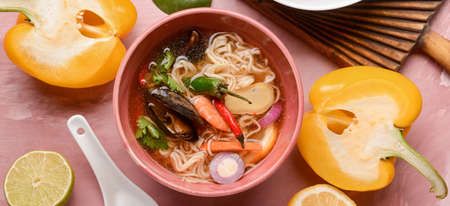 Bowl of spicy Thai soup on pink background