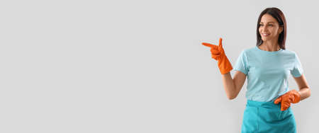 Young woman in rubber gloves pointing at something on light background with space for textの写真素材
