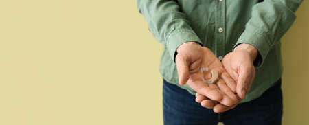 Man holding hearing aid on color background with space for text, closeupの写真素材