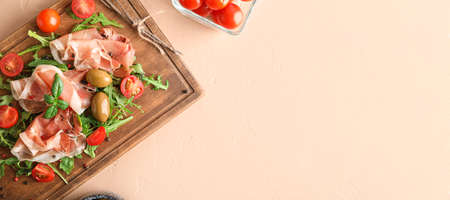 Wooden board with delicious jamon, spices, olives and tomatoes on light background with space for...