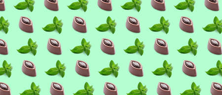 Many tasty chocolate candies and mint on green background. pattern for designの写真素材