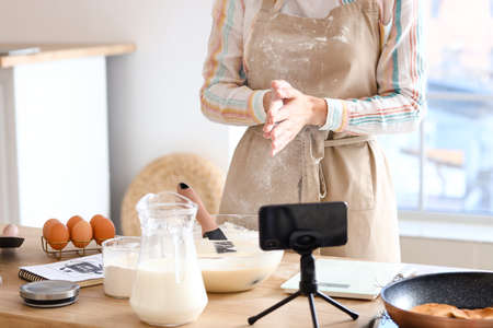 Young woman making dough for pancakes while following video tutorial in kitchen