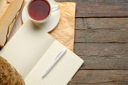 Notebook, old paper, cup of tea and pen on wooden backgroundの写真素材
