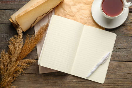 Notebook, old paper, cup of tea and pen on wooden background, top viewの写真素材