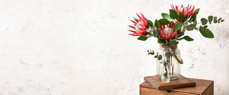 Vase with bouquet of protea flower on table near light wall in room