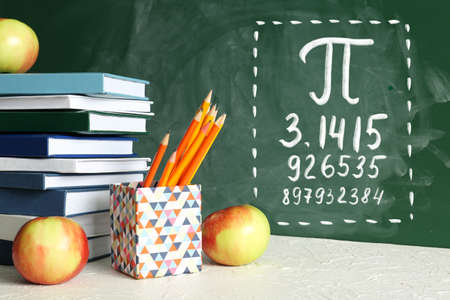 Set of school stationery and apples on table near blackboard with written number Piの写真素材