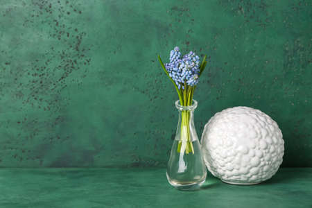Vase with beautiful Muscari flowers and decor on green background