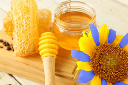 Jar of honey and sunflower in colors of Ukrainian flag on table, closeup