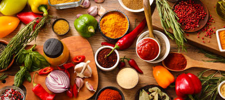 Different aromatic spices with fresh herbs, vegetables and sauce on wooden background, top viewの写真素材