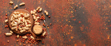 Board, tasty peanut butter and nuts on grunge background with space for text