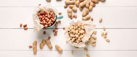 Cups with tasty peanuts on white wooden background