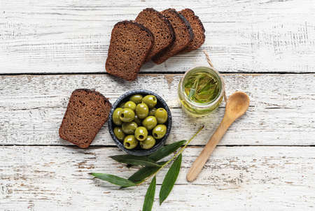 Composition with bowl of green olives, oil and bread on light wooden background