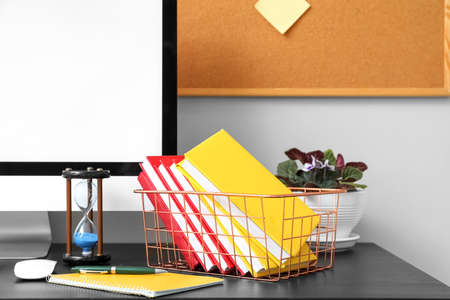 Basket with books, hourglass, computer and houseplant on table near light wallの写真素材