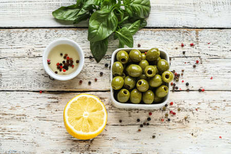 Composition with bowl of green olives, oil, lemon and spices on light wooden background