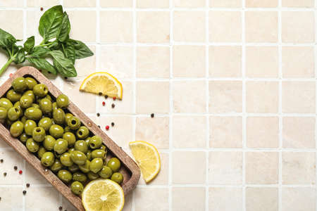 Composition with wooden board of green olives and lemon on light tileの写真素材