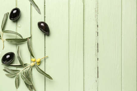 Tasty black olives and leaves on color wooden background