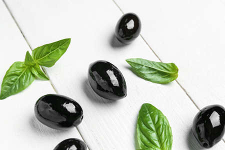 Tasty black olives with basil on light wooden background, closeupの写真素材
