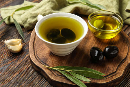 Board with bowls of oil and olives on wooden table, closeupの写真素材