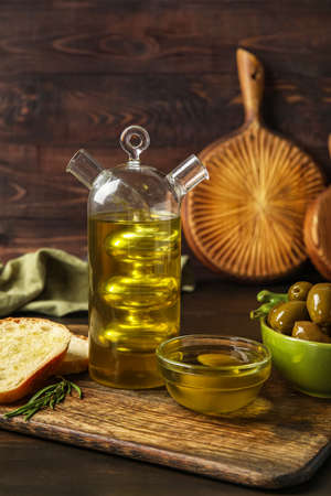 Board with bottle of fresh oil, bread and olives on dark wooden tableの写真素材