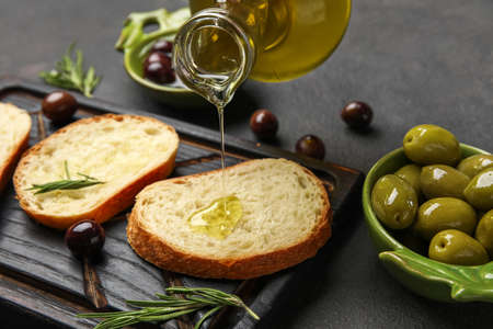 Pouring of olive oil onto fresh bread on dark background, closeupの写真素材